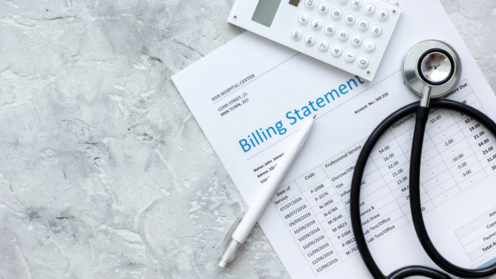 A stethoscope, a pen, a calculator, and a billing statement lie on a light gray marble surface. The billing statement is partially visible with several medical charges listed. Prominently featuring medical billing and coding, the calculator has a blank screen, and the pen is placed diagonally across the paper.